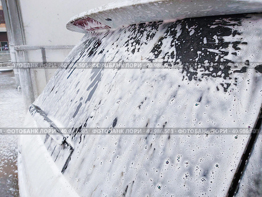 The back of the very dirty white SUV, doused with shampoo and foam, stands in the  box of outdoor self-service car wash and waits for washing. Очень грязный белый внедорожник, облитый шампунем и пеной, стоит в боксе уличной автомойки самообслуживания и ждет мойки. Стоковое фото, фотограф Дмитрий Березнев / Фотобанк Лори