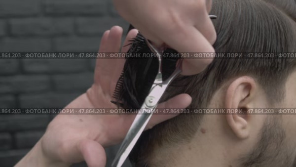 The barber picks up a lot of hair with his fingers and cuts off the ends with scissors. He makes the man's haircut look new. Стоковое видео, видеограф Strunov David / Фотобанк Лори