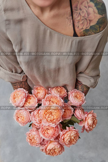 The beautiful bouquet of flowers in the girls hands with tatoo on a gray background. Top view.. Young woman with a tattoo on her shoulder with a bouquet of pink Buttercup in her hands. Стоковое фото, агентство Ingram Publishing / Фотобанк Лори