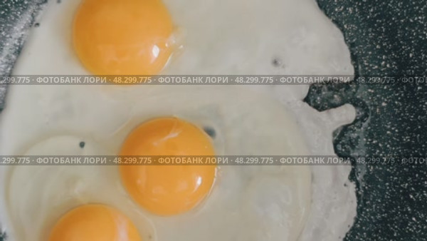 The egg sizzles as it hits the hot pan, the clear liquid slowly turning white and firm around the bright yellow yolk. Стоковое видео, видеограф Алексей Круковский / Фотобанк Лори