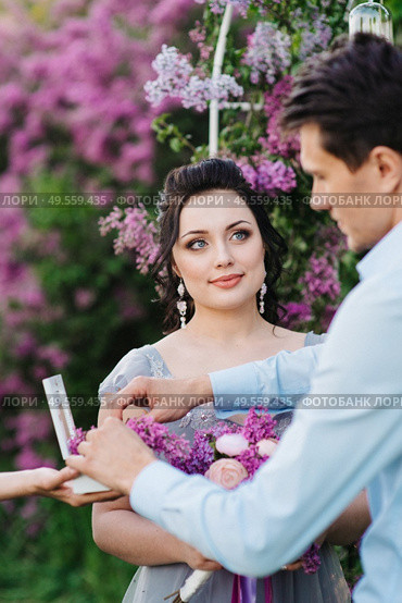 the groom dresses the bride with wedding rings near the lilac arch. Стоковое фото, агентство Ingram Publishing / Фотобанк Лори