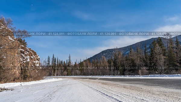 The highway goes around a cliff with steep slopes. Trees grow in snowdrifts on the roadsides. A mountain range against the blue sky. Altai. Chuysky tract. Стоковое фото, фотограф Вера Ивановна Кубарева / Фотобанк Лори