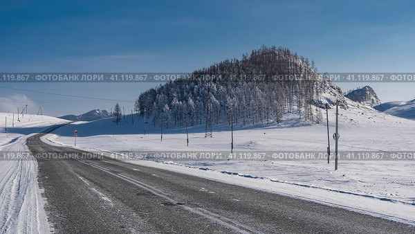 The highway runs through a snow-covered valley. On the hill there is a coniferous forest covered with frost. Mountains ahead, against a clear blue sky. Altai. Chuysky trakt. Стоковое фото, фотограф Вера Ивановна Кубарева / Фотобанк Лори