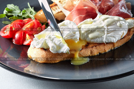 The knife cuts the Eggs Benedict on toasted bread with ham, tomatoes and sauce. Eggs Benedict on toasted with ham and sauce. Стоковое фото, агентство Ingram Publishing / Фотобанк Лори