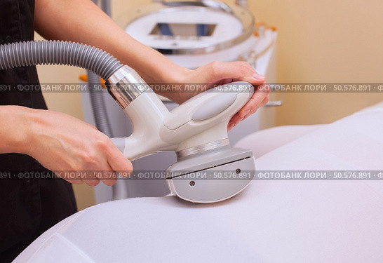 The masseur makes an hardware massage on the patient’s ass and legs in a white suit, close-up in a beauty salon. Стоковое фото, агентство Ingram Publishing / Фотобанк Лори