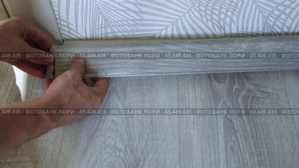 The master finisher installs a plastic baseboard, snapping it into the grooves. Home renovation. Стоковое видео, видеограф Дмитрий Кобзев / Фотобанк Лори