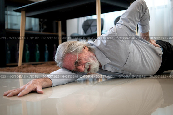The old man fell down in the living room inside the house. have to take care of themselves without their children taking care of them have severe back pain. Стоковое фото, агентство Ingram Publishing / Фотобанк Лори