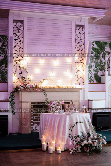 The presidium of the newlyweds in the banquet hall of the restaurant is decorated with candles and green plants, wisteria hangs from the ceiling. Стоковое фото, агентство Ingram Publishing / Фотобанк Лори