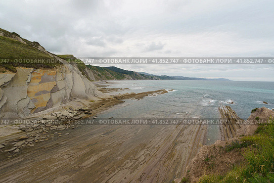 The seascape in Basque Autonomous Community in summer cloudy day. Wide Atlantic ocean beach surrounded by mountains at low tide in Bay of Biscay. Charming Zumaia Algorri beach. Стоковое фото, фотограф YuryKara / Фотобанк Лори