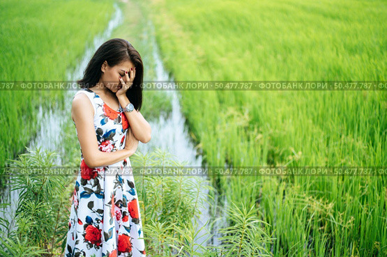 The woman stood strained and her hand closed her face in the meadow. Стоковое фото, агентство Ingram Publishing / Фотобанк Лори