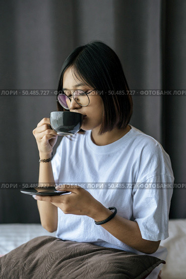 There was a girl sitting and drinking coffee in the bedroom and a pillow on her legs. Стоковое фото, агентство Ingram Publishing / Фотобанк Лори