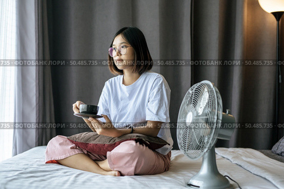 There was a girl sitting and drinking coffee in the bedroom and a pillow on her legs. Стоковое фото, агентство Ingram Publishing / Фотобанк Лори