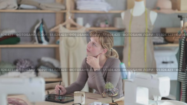 Thoughtful female fashion designer sitting at work table in studio. Стоковое видео, видеограф Яков Филимонов / Фотобанк Лори