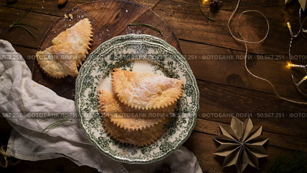 Three golden brown pastries dusted with powdered sugar on a vintage plate with a festive Christmas backdrop. Стоковое фото, агентство Ingram Publishing / Фотобанк Лори