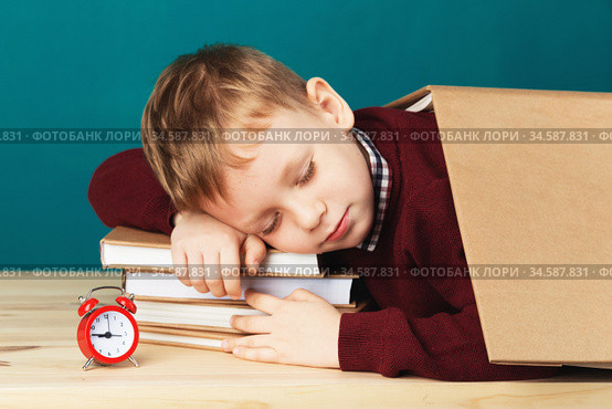 tired school boy asleep on books. little student sleeping on textbooks. Child in school uniform lies on the table with big pile of books against blue wall. Eyes closed. School concept. Стоковое фото, фотограф Nataliia Zhekova / Фотобанк Лори