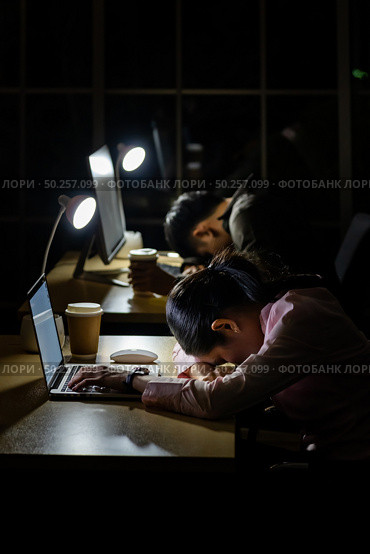 Tired young asian businesswoman and businessman sleeping at computer desk in office late ay night. Стоковое фото, агентство Ingram Publishing / Фотобанк Лори