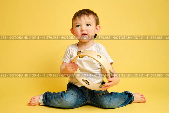 Toddler baby plays the tambourine, a child with a percussion musical instrument on a studio yellow background. Happy child musician playing hand drum. Kid aged one year four months. Стоковое фото, фотограф Андрей Журавлев / Фотобанк Лори
