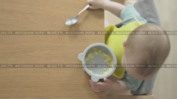 top view baby eating himself holding teaspoon from silicone plate sitting table. Стоковое видео, видеограф Olesia Kondrateva / Фотобанк Лори