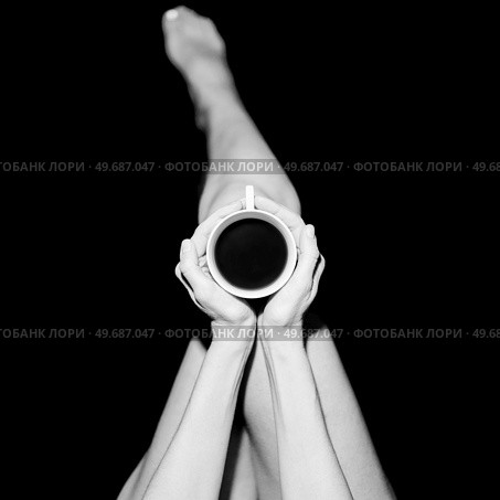 Top view of crop unrecognizable barefooted female sitting in black studio with cup of hot coffee. Crop anonymous woman with coffee cup in black studio. Стоковое фото, агентство Ingram Publishing / Фотобанк Лори
