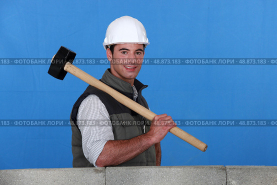 Tradesman holding a mallet and standing behind a low wall. Стоковое фото, агентство Ingram Publishing / Фотобанк Лори