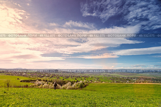 Traveler on green spring meadow. Village on sunny green spring foothills. Orchard blooming on hills. Sunny green blooming spring landscape. Стоковое фото, агентство Ingram Publishing / Фотобанк Лори