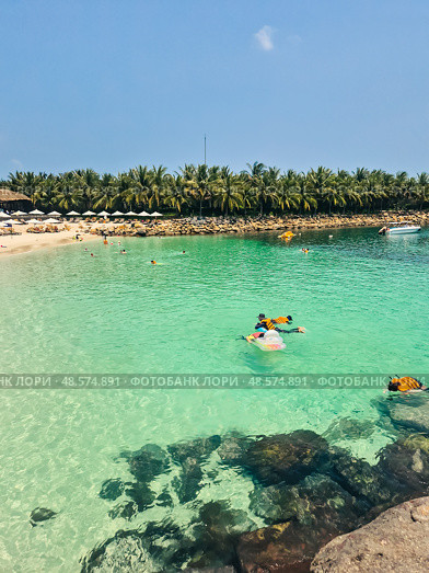 Tropical beach scene in Vietnam with swimmers in life jackets, crystal clear water, horizon view, white sand, rocks and palm trees. Nha Trang coastline. Стоковое фото, фотограф Татьяна Терехина / Фотобанк Лори