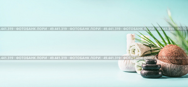 Tropical spa setting background with coconut, palm leaves at light blue. Massage treatment. Rolled towels, compress balls and hot stone. Beauty, wellness and body care. Banner or template. Copy space. Стоковое фото, агентство Ingram Publishing / Фотобанк Лори