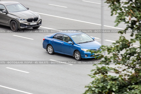 Two cars in motion on city street. Toyota corolla and BMW X5 racing at high speed on urban avenue. Compliance with speed limits on the road. Редакционное фото, фотограф Константин Григорьев / Фотобанк Лори