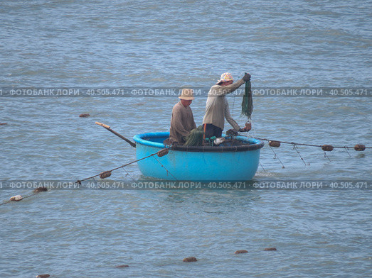 Two fishermen sail in a traditional Vietnamese boat. One of them throws the net. (2015 год). Редакционное фото, фотограф Ирина Кононова / Фотобанк Лори