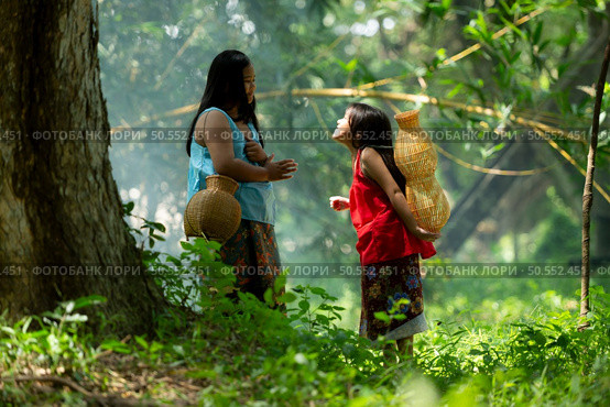 Two girls Asian women with traditional clothing stand in the rainforest. They had fun playing together before assisting Grandpa in catching fish in a nearby lake. Стоковое фото, агентство Ingram Publishing / Фотобанк Лори