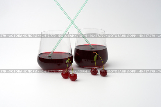 Two glasses of cherry straw drink on a white background. Next to them are paired cherry berries on peduncles. Copy space. Стоковое фото, фотограф Роман Дзюбало / Фотобанк Лори