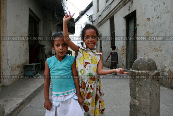 Two little black Arab girl standing on a narrow street. Стоун Таун - Каменный город на острове Занзибар, две десятилетние девочки  гримасничают и кривляются перед туристами с фотокамерами. (2008 год). Редакционное фото, фотограф Владимир Григорьев / Фотобанк Лори