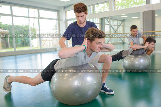Two men assisting friends exercising on aerobic balls. Стоковое фото, агентство Ingram Publishing / Фотобанк Лори