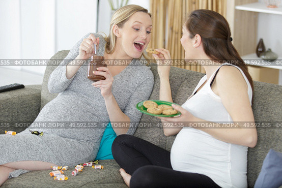 two pregnant women friends eating bad food at home. Стоковое фото, агентство Ingram Publishing / Фотобанк Лори