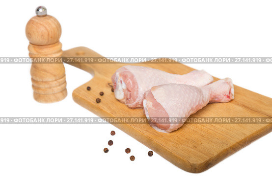 Two raw chicken drumsticks on a cutting board and peppermill on a white background. Стоковое фото, фотограф Юлия Бабкина / Фотобанк Лори