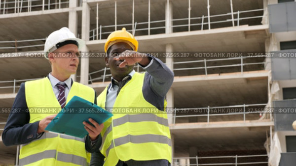 Two successful architects standing on the construction site are discussing the construction plan, holding drawings in their hands. Стоковое видео, видеограф Яков Филимонов / Фотобанк Лори