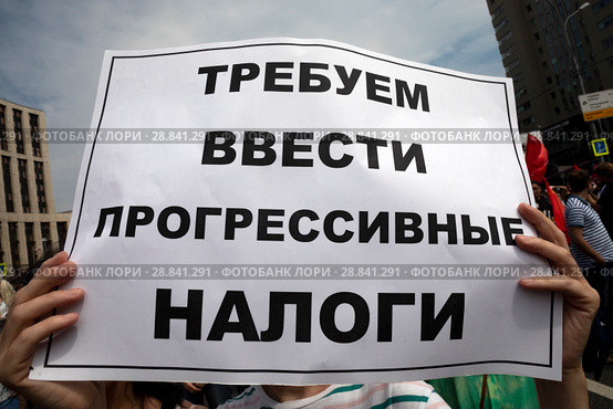 Участник митинга КПРФ на проспекте Сахарова держит плакат с требование ввести прогрессивные налоги в городе Москва, Россия (2018 год). Редакционное фото, фотограф Николай Винокуров / Фотобанк Лори