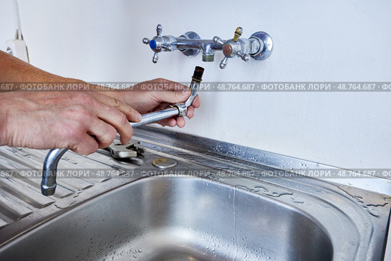 Unscrewing old faucet spout from wall tap fitting as part of faucet replacement process with hand and tool positioned above stainless sink. Стоковое фото, фотограф Владимир Григорьев / Фотобанк Лори