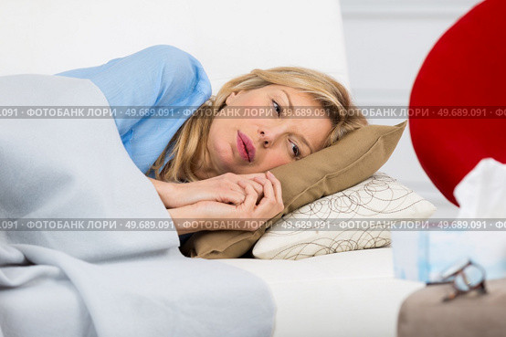 unwell woman laying on couch at home. Стоковое фото, агентство Ingram Publishing / Фотобанк Лори