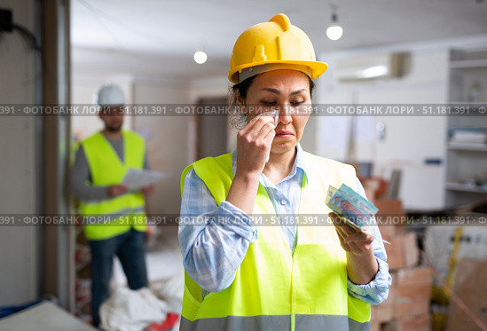 Upset female builder standing in building under renovation with money. Стоковое фото, фотограф Яков Филимонов / Фотобанк Лори