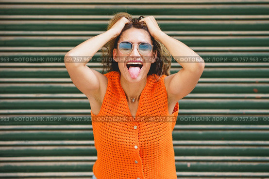 Urban portrait of a casual latin cool woman holing her hair and sticking the tongue out smiling. Woman holing her hair and sticking the tongue out smiling. Стоковое фото, агентство Ingram Publishing / Фотобанк Лори