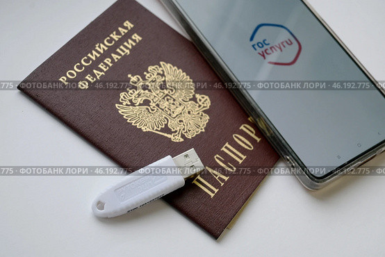 Устройство  USB eToken  (рутокен) белого цвета, устройство для хранения электронной цифровой подписи (ЭЦП) и информации для аутентификации пользователя, паспорт и телефон с приложением Госуслуги на белом фоне. Редакционное фото, фотограф Snezka / Фотобанк Лори