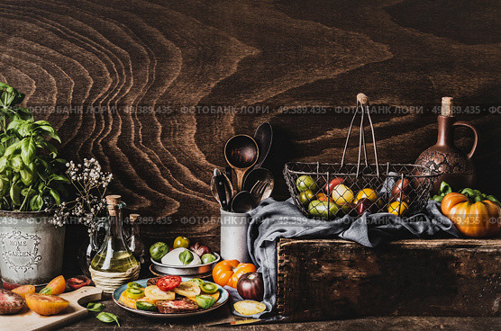 Various colorful tomatoes from garden, salad in plate, olives oil , mozzarella and kitchen tools on dark rustic table, front view. Still life. Стоковое фото, агентство Ingram Publishing / Фотобанк Лори