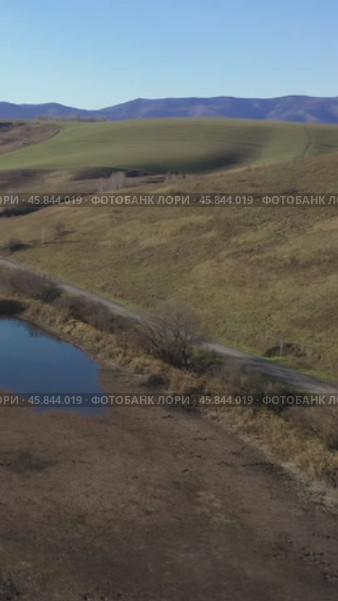 Vertical drone video of flying over a hilly rural landscape with a winding road and fish ponds. Altai Krai. Стоковое видео, видеограф Сергей Пристяжнюк (Serg Zastavkin) / Фотобанк Лори