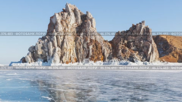Video of winter Baikal Lake. View of famous Shamanka Rock or Cape Burkhan - natural landmark of Olkhon Island. Scenic winter landscape with blue ice on sunny day in February. Travels and recreation. Стоковое видео, видеограф Виктория Катьянова / Фотобанк Лори