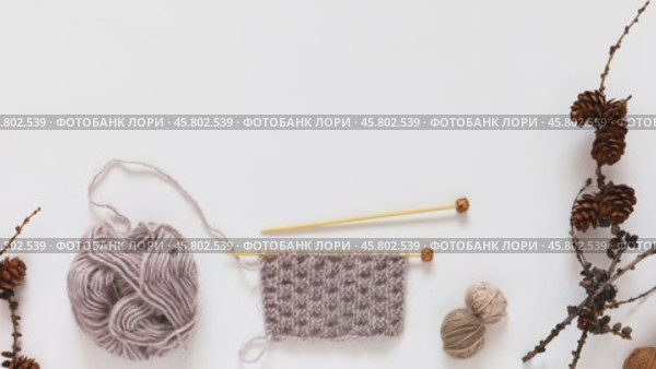 Video of winter knit and needlework. Knitting a warm scarf from soft beige wool yarn. Nearby are woolen balls and dry larch tree branches with cones on white background. Flat lay, top view, mock up. Стоковое видео, видеограф Виктория Катьянова / Фотобанк Лори