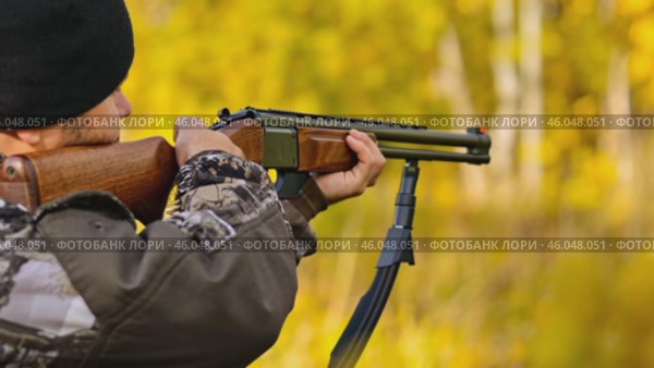 View from behind the shoulder of a man in camouflage uniform, with a gun on his shoulder and a cartridge, who hunts in the autumn forest. Стоковое AI-видео, аниматор Ирина Старикова / Фотобанк Лори
