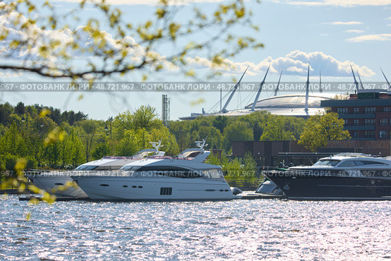 View of the mega yachts standing at the pier through the branches of trees on a clear sunny day, residential buildings and a stadium in the background, Russia, St.Petersburg. Стоковое фото, фотограф Vladimir Drozdin / Фотобанк Лори
