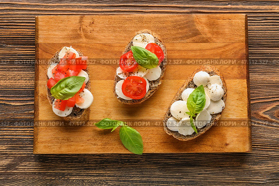 Вкусные бутерброды с моцареллой, помидорами и базиликом на деревянной доске. Стоковое фото, фотограф Pixel_shot / Фотобанк Лори