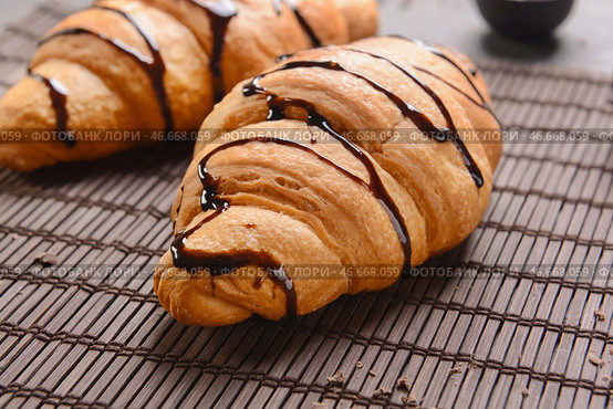Вкусные круассаны с шоколадным сиропом на бамбуковой циновке. Стоковое фото, фотограф Pixel_shot / Фотобанк Лори